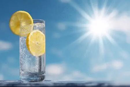 Visoka čaša vode s limunom na jakom suncu simbolizirajući hidrataciju za brzo smanjenje razine bilirubina