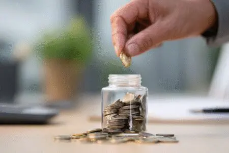 Ruka ubacuje kovanice u staklenku kao prikaz poreza i doprinosa za paušalni obrt
