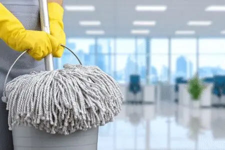 Ruke drže čistu krpu i kantu a u pozadini je uredan prostor kao prikaz za kako otvoriti obrt za čišćenje