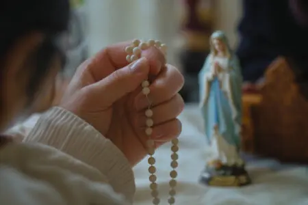 prikaz kako se moli gospina krunica s rukama u molitvi ispred kipa djevice marije