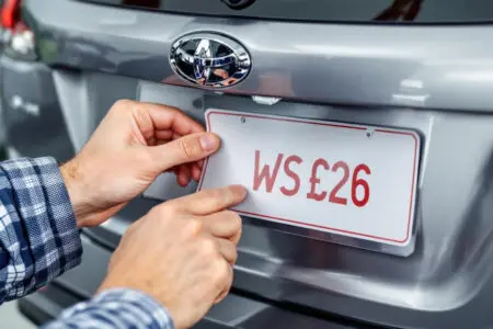 ruke postavljaju privremenu papirnatu registarsku oznaku na novi automobil što prikazuje probne tablice