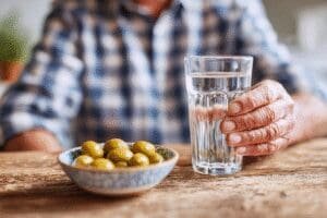 Osoba pije čašu vode pored zdjelice sa slanim maslinama što simbolizira sigurne metode za povišenje niskog krvnog tlaka
